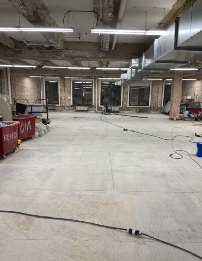 image shows a large, empty room with concrete floors and exposed ceiling pipes and ductwork