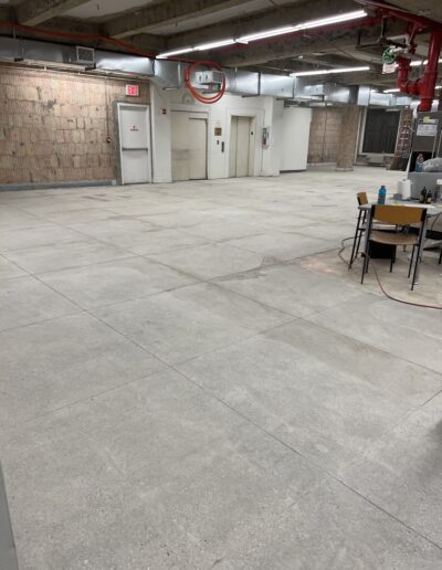 image shows a large, empty room with concrete floors and exposed ceiling pipes and ductwork